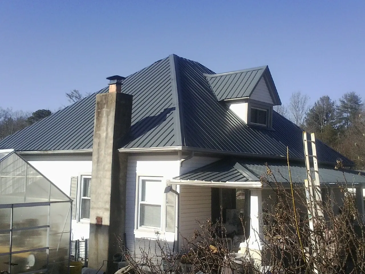 Dark blue standing seam metal roof on a white farmhouse with dormer — Slate & Tile Roof Repair by Roofing Brothers in Wise