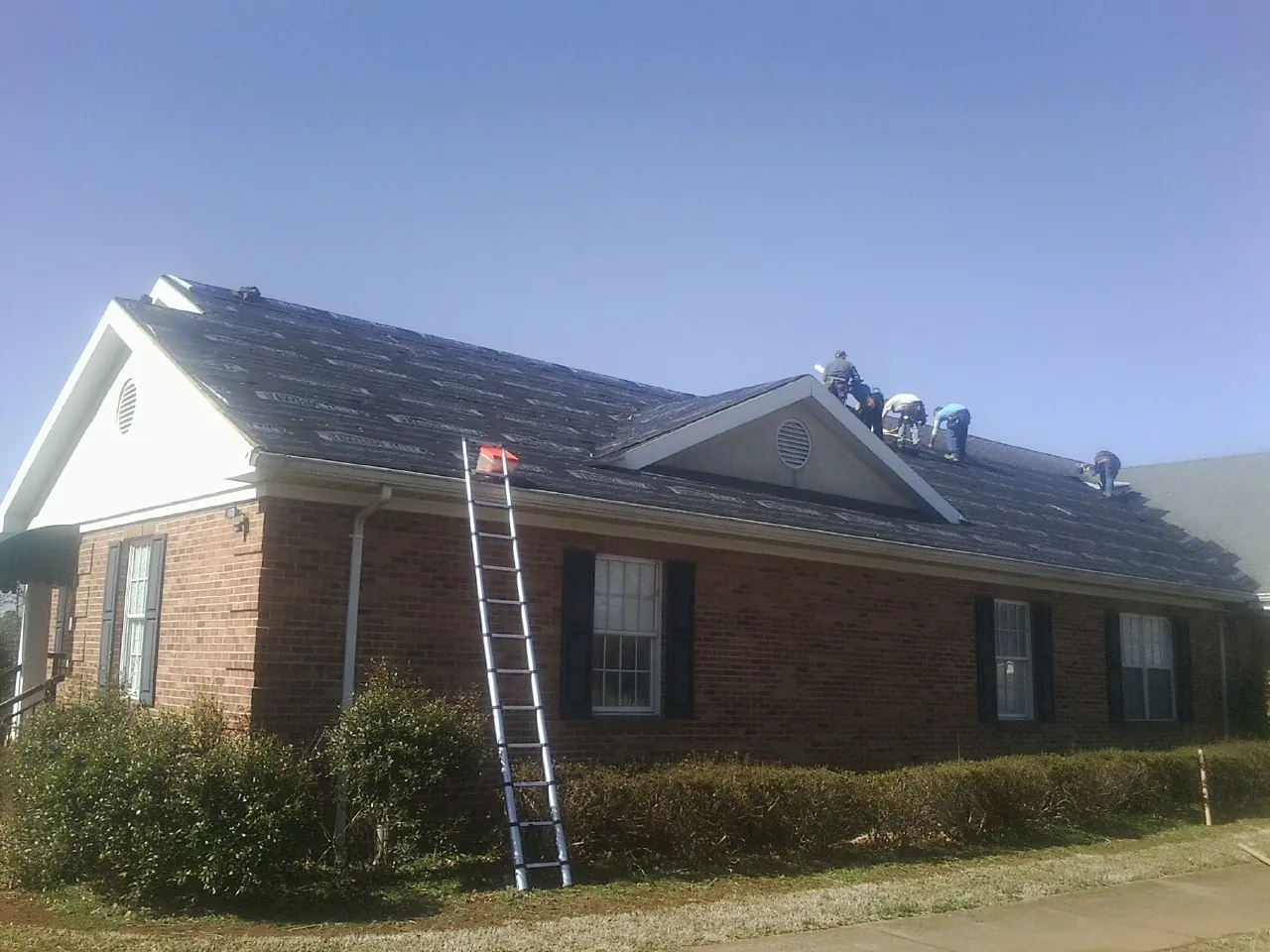 Crew tearing shingles off a brick ranch roof with a ladder set — Metal Roof Repair work by our crew in Wise