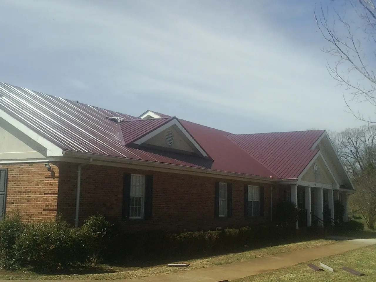 Red metal roof with gabled entries on a long brick building, from a Hail Damage Roof Repair job in Wise