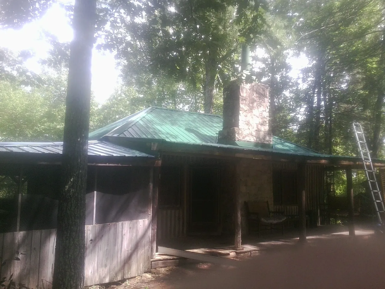 Green metal roof and stone chimney above a log cabin porch in Wise